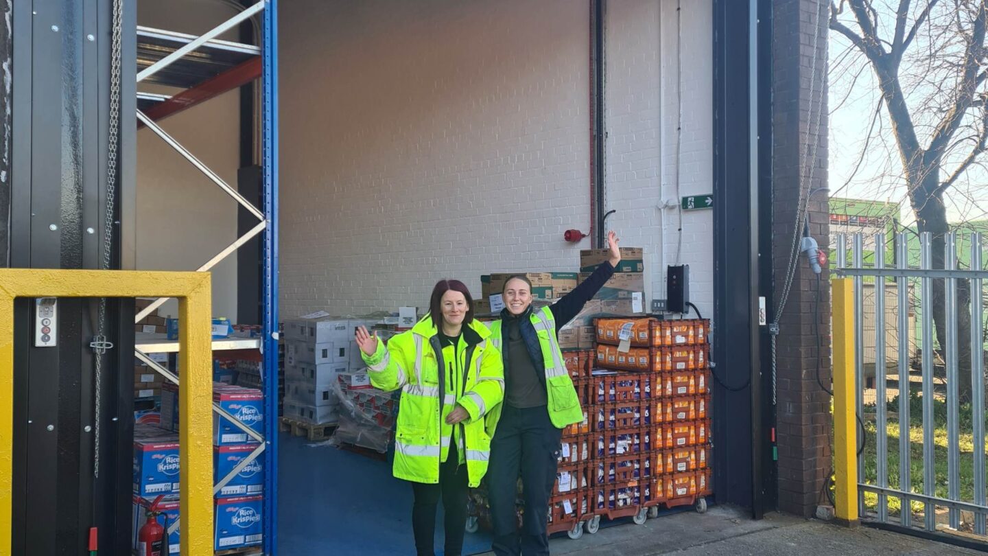 Two warehouse staff members stand outside their new premises