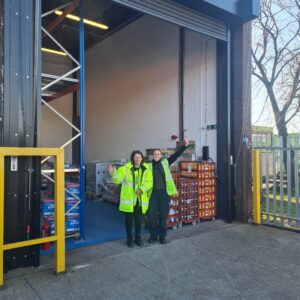Two warehouse staff members stand outside their new premises where they serve surplus food to local charities