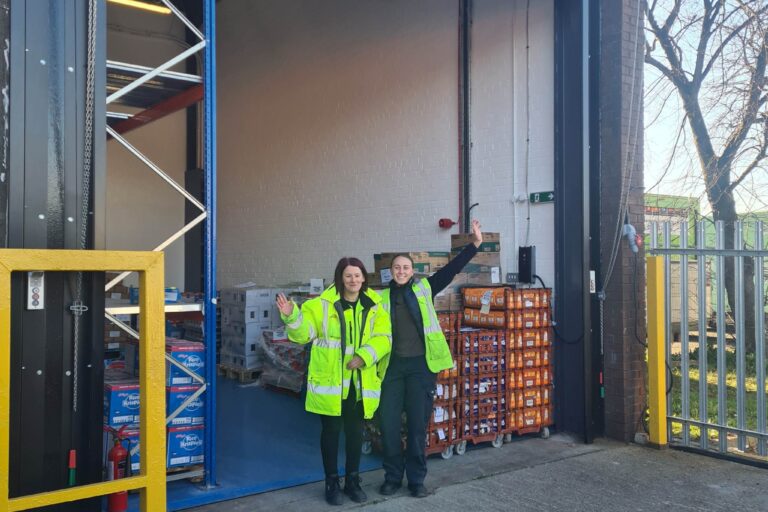 Two warehouse staff members stand outside their new premises