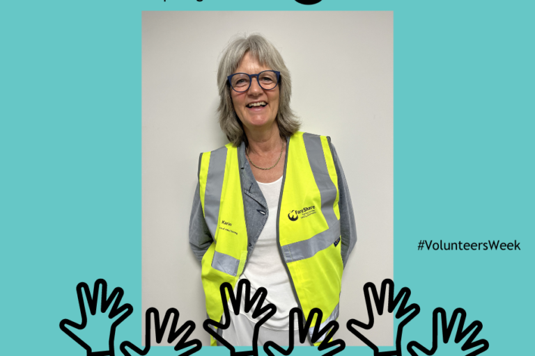 Karin standing against a white wall wearing a FareShare hi viz vest
