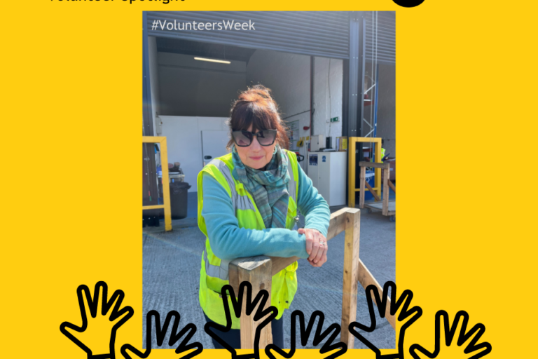 Sally, a FareShare Plus volunteering wearing high visibility vest & standing in the yard leaning on a trolley
