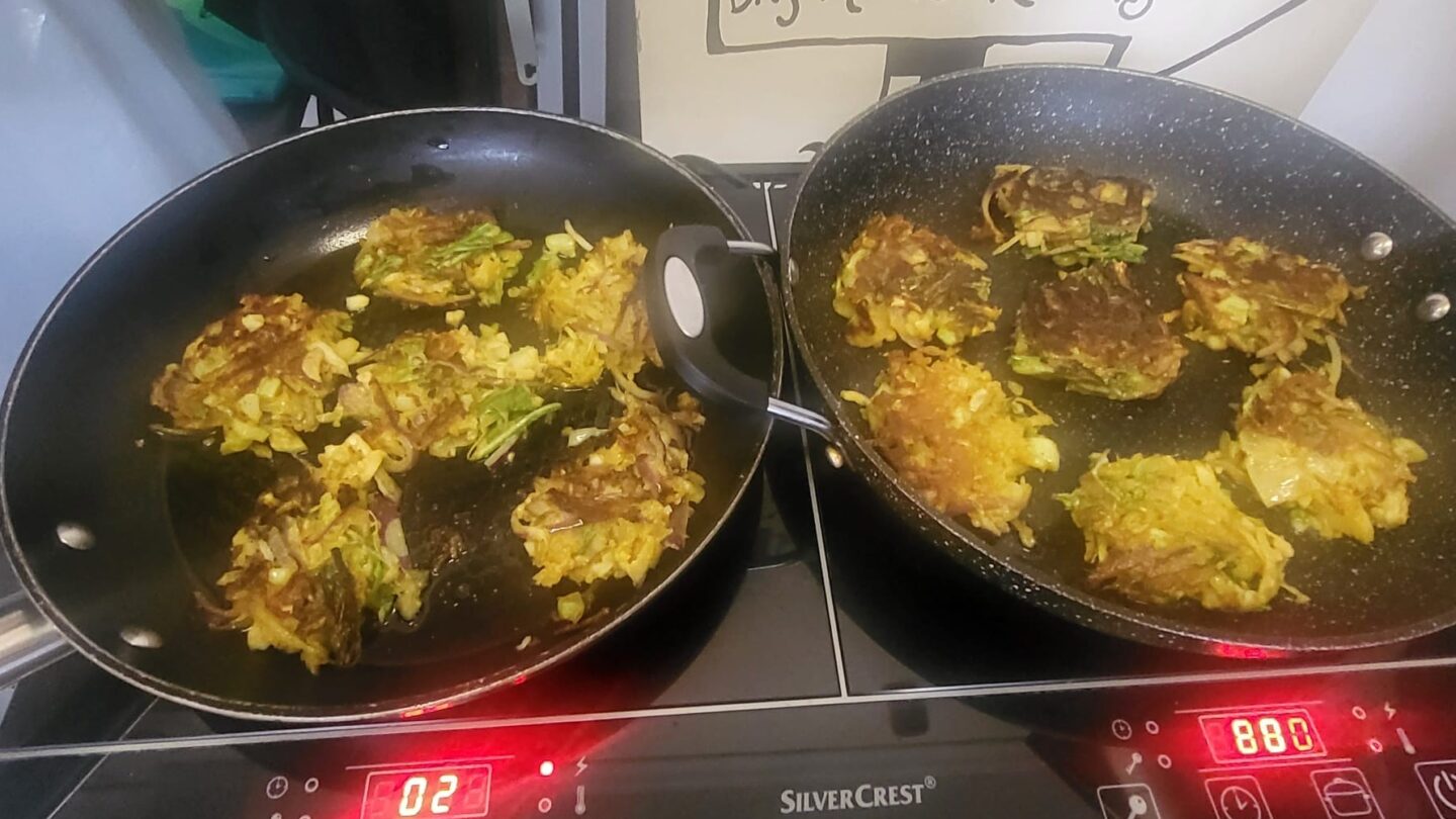 Close up of two frying pans each on the hob with cauliflower bhajis cooking