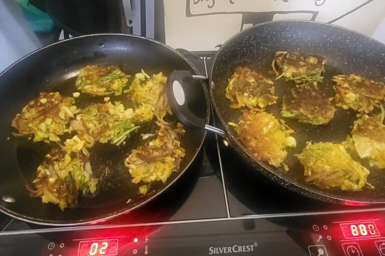 Close up of two frying pans each on the hob with cauliflower bhajis cooking