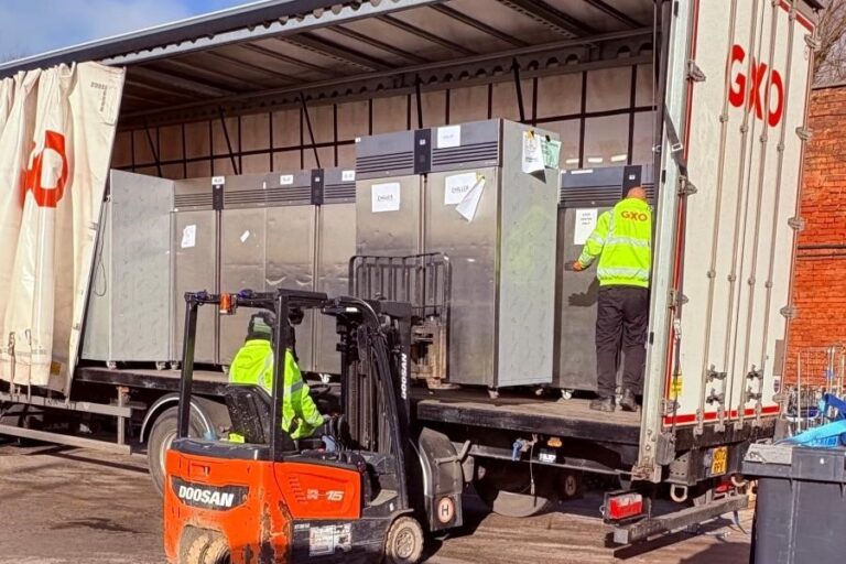 forklift taking a large fridge off the back of a large lorry