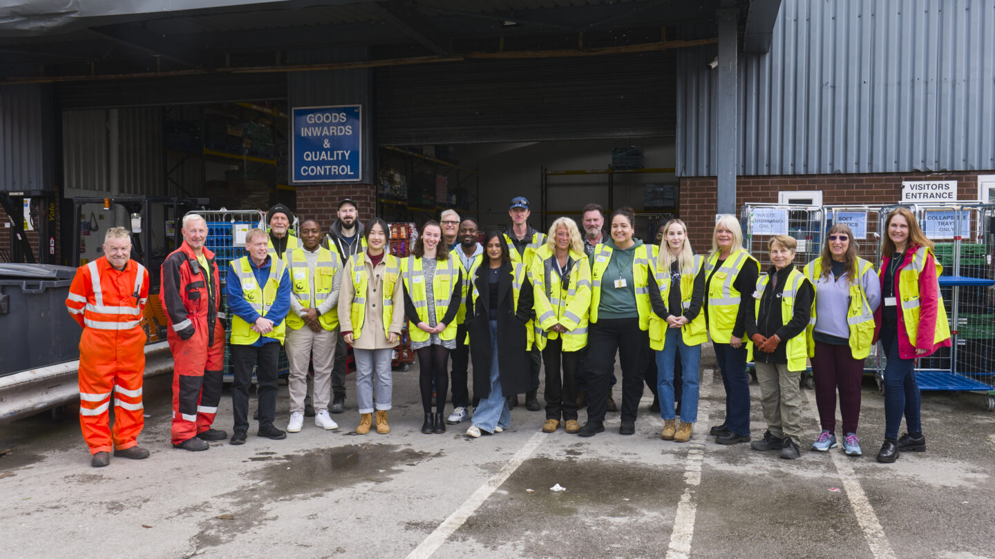 Image shows group photo of FareShare Greater Manchester staff and volunteers standing in the goods yard outside the open warehouse doors