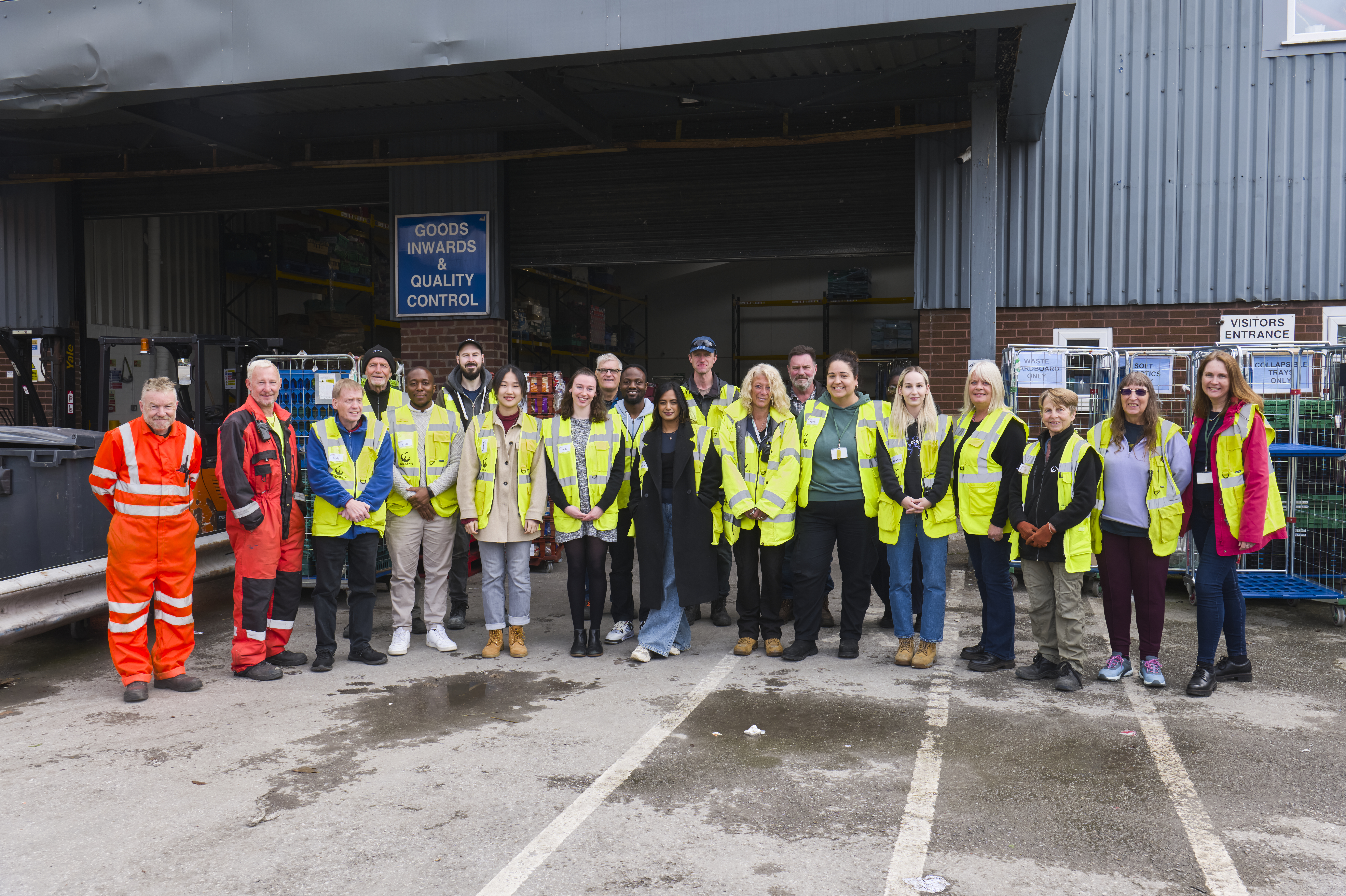 Image shows group photo of FareShare Greater Manchester staff and volunteers standing in the goods yard outside the open warehouse doors